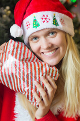 Christmas portrait of happy young woman holding a wrapped gift/present wearing Santa hat.
