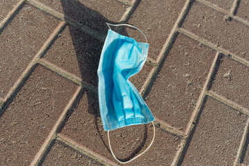 Used medical face mask left on ground pavement - Environmental pollution. 