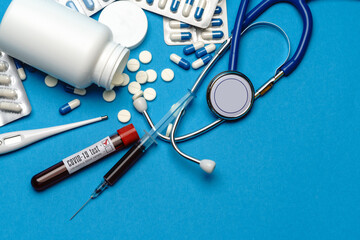 Stethoscope, syringe, thermometer, blood test tube and can of pills on blue background top view with copy space