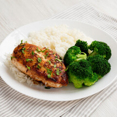 Homemade Chicken Breast, Rice and Broccoli on a white plate on a white wooden table, side view. Close-up.