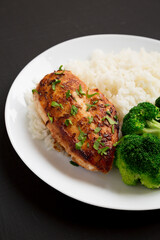 Homemade Chicken Breast, Rice and Broccoli on a white plate on a black background, side view. Close-up.