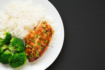 Homemade Chicken Breast, Rice and Broccoli on a white plate on a black surface, top view. Flat lay, overhead, from above. Space for text.