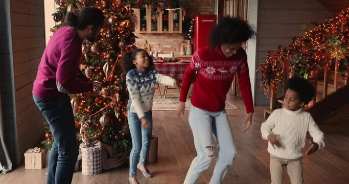 Happy african family spouses and children gathered in living room decorated with twinkled lights Christmas tree listen funky music dancing enjoy winter holidays. New Year celebration, pastime concept