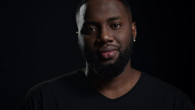 Relaxed afro guy looking at camera indoors. Smiling male person posing in studio