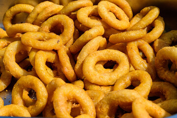 Large group of freshly fried calamari and onion rings on display for sale at a street food festival, ready to eat healthy seafood, beautiful orange monochrome outdoor background.