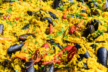 Close up of large portion of traditional Spanish paella dish freshly being cooked with seafood and rice in a frying pan at a street food festival, ready to eat seafood, side view, selective focus.