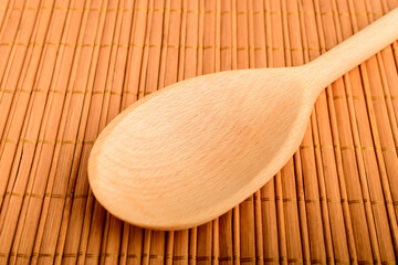 One raw brown wooden spoon on a wooden surface on a table at home, in warm light, diagonally displayed, brown monochrome indoor background.