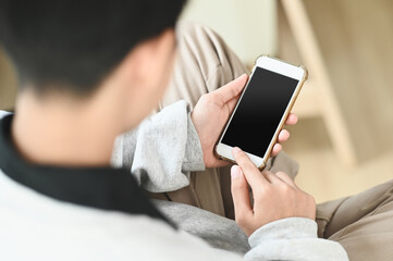 Happy casual beautiful woman is using smartphone with white screen and sitting on a sofa at home.
