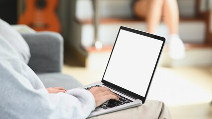 Cropped shot of a young female working with white screen laptop while sitting on sofa at home.