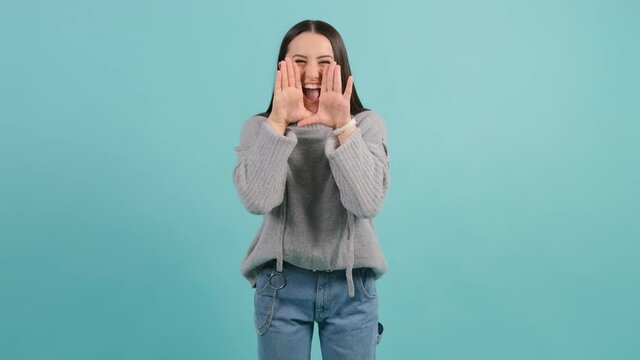 Young woman that is shouting angry out loud with hands over mouth, isolated over turquoise background.