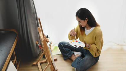 A young woman artist painting at home creative while sitting on floor at home.