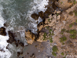 Aerial top down photo of foaming waves crashing against rocky shore, big stones on coastline. Aegean sea, nature of Crete, Greece. Sea natural patterns, background wallpaper.