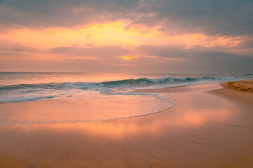 Beautiful ocean beach at sunset. Foamy waves over wheat sand and beautiful cloudy sky.