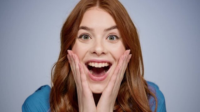 Joyful girl making hand gestures in studio. Female person touching face indoors