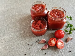 homemade delicious ketchup in a glass jar and its organic ingredients on burlap