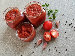 homemade delicious ketchup in a glass jar and its organic ingredients on burlap