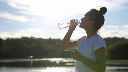 Girl quench their thirst on a hot sunny day after a jog, drink water. Healthy lifestyle.Woman in the Open air Drinks Water from a Bottle