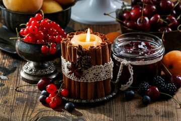 Candle decorated with cinnamon sticks among autumn fruits on the wooden table.