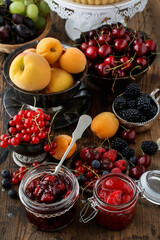 Jar of cherry jam among summer and autumn fruits on a wooden table.