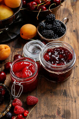 Jar of cherry jam among summer and autumn fruits on a wooden table.