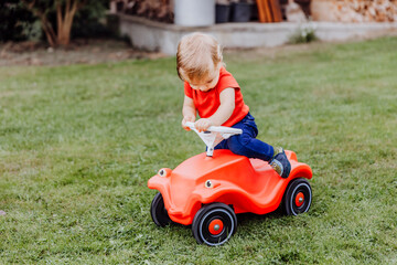 Baby girl getting on toy car in garden