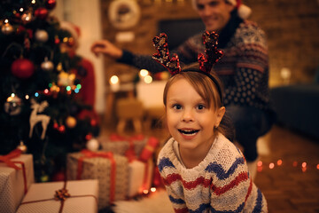 Cute little girl wearing reindeer antlers on Christmas eve at home.