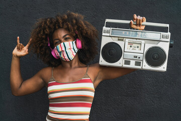 Young Afro woman wearing face mask dancing outdoor while listening to music with wireless...