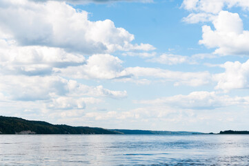 Obraz premium beautiful peacful landscape of water, hills with trees and blue sky with clouds on river