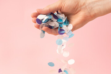 White, lilac and blue confetti in a woman's hand on a pink background
