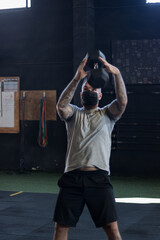 Chico con mascarilla en un gimnasio realizando Cross training con mancuernas