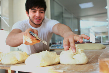 The person is out of focus. A young Baker cuts yeast dough into portions. The concept of cooking bakery products. Indoors. Close up.
