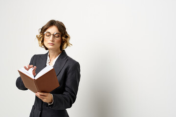 Woman at work with book in hand light background classic suit glasses head