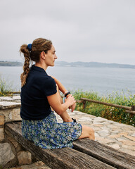 Girl looking to the ocean sitting on a beautiful bench. Side view