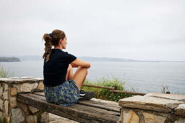 Girl looking to the ocean sitting on a beautiful bench
