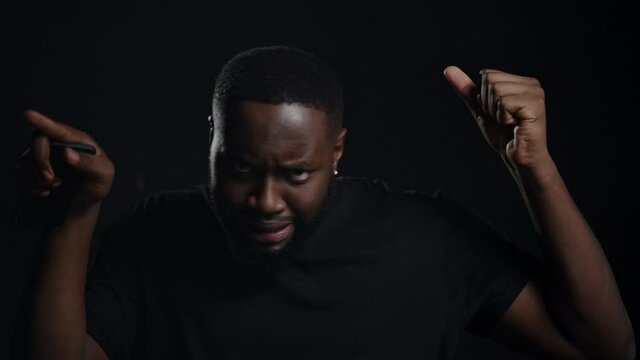 Friendly guy doing movements on black background. Man making gestures indoors