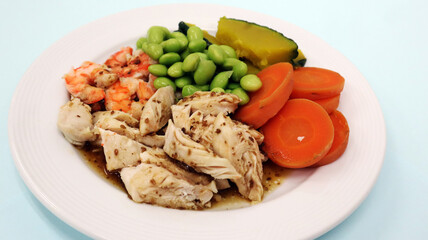 Clean meal and keto food with chicken and shrimps seasoning with sesame sauce healthy for diet dining, eat with vegetables, carrot, beans and pumpkin. Put on the white plate isolated in blue table.