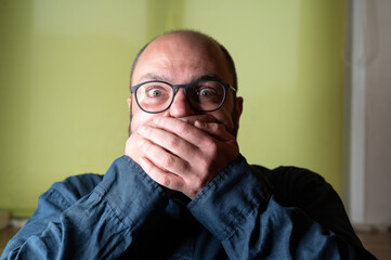 Man covers his mouth with both hands and looks scared into the camera