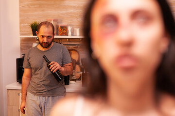 Abusive husband drinking alcohol looking at traumatised wife because of his domestic violence....