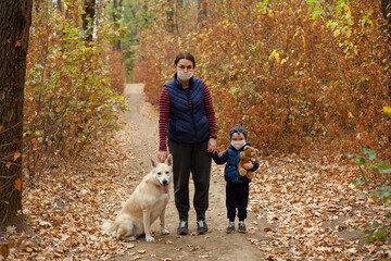 Naklejka na ściany i meble Mom and daughter in masks walk in the woods with a dog.