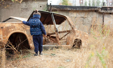 Obraz premium Little girl near the burned-out car. War in Donetsk. War Nagorno-Karabakh. Burned-out car.