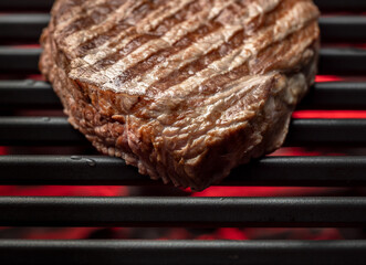 Beef steak cooking on grilled with red coals flame, top view. Traditional fried meat with diagonals lines on a bbq party in American style.