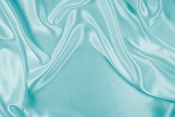 Photography of beautiful wavy turquoise silk satin luxury cloth fabric, abstract background design.