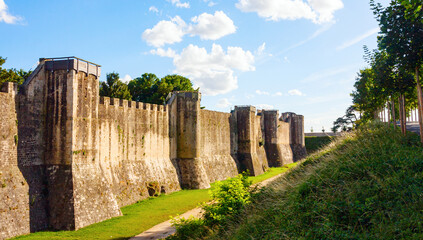 Fototapeta na wymiar Medieval city wall reinforced with towers and a deep moat under a blue sky with clouds during sunset. Provins, Seine-et-Marne, France.