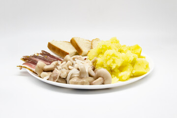 Pickled butter mushrooms with onions on a plate with bacon, potatoes and slices of bread isolated on a white background. Delicious Ukrainian meal for lunch or dinner.