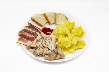 Pickled butter mushrooms with onions on a plate with bacon, potatoes and slices of bread isolated on a white background. Delicious Ukrainian meal for lunch or dinner.