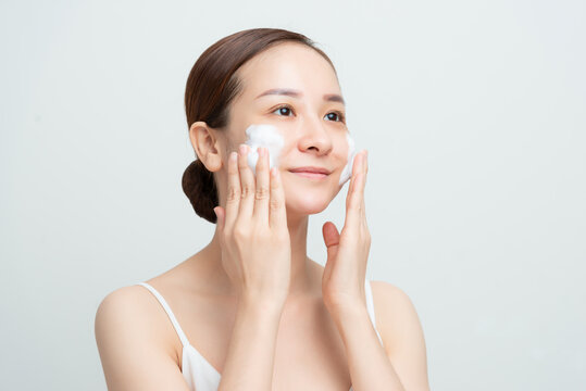 Face skin care. Woman applying facial cleanser on face closeup. Girl using cleansing cosmetic product on skin, washing face on light background