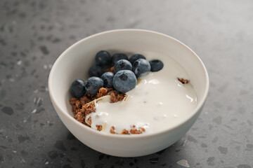Healthy breakfast with whole grain granola and fresh blueberries in white bowl on concrete background
