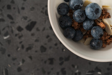 Healthy breakfast with whole grain granola and fresh blueberries in white bowl on concrete background