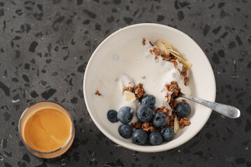 Healthy breakfast with whole grain granola and fresh blueberries in white bowl with coffee on concrete background