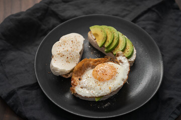 Three ciabatta slices with fried egg, avocado and mozzarella on black plate